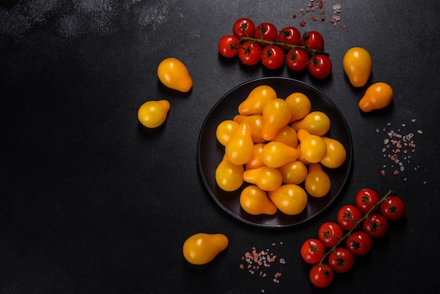 Petites tomates jaunes en forme de poire dans une assiette en céramique sur une table en béton foncé