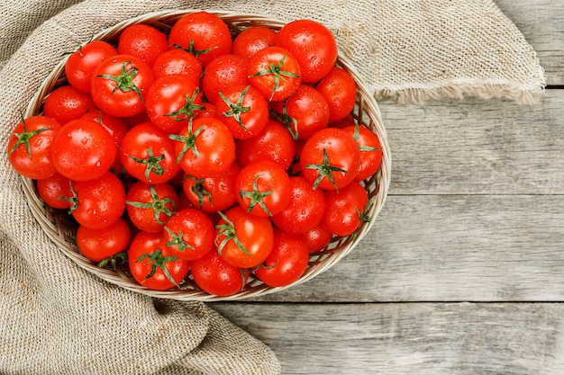 Petites tomates rouges dans un panier en osier sur une vieille table en bois. Cerise mûre et juteuse