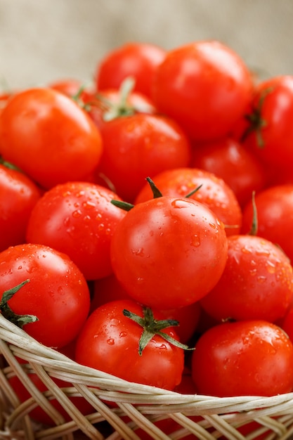 Petites tomates rouges dans un panier en osier sur une vieille table en bois. Cerise mûre et juteuse