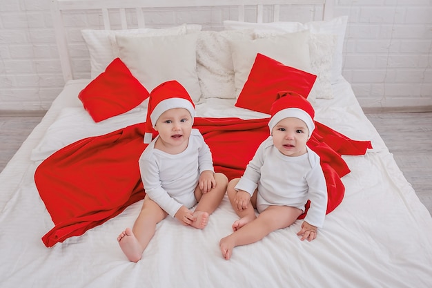 petits beaux enfants un garçon et une fille sont assis sur le lit dans des chapeaux de Noël