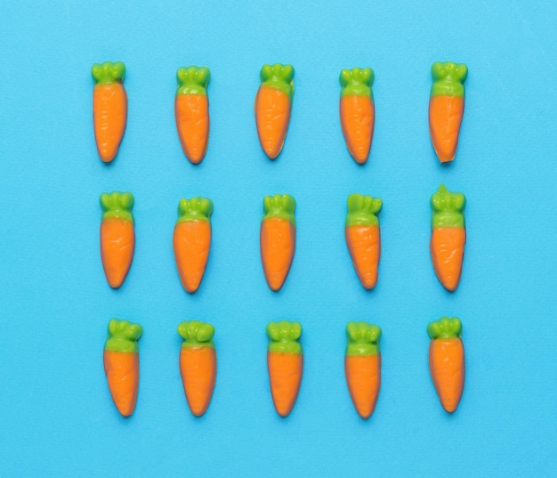 Petits bonbons sous forme de carottes empilées en trois rangées sur fond bleu Concept de récolte minimal Photo créative