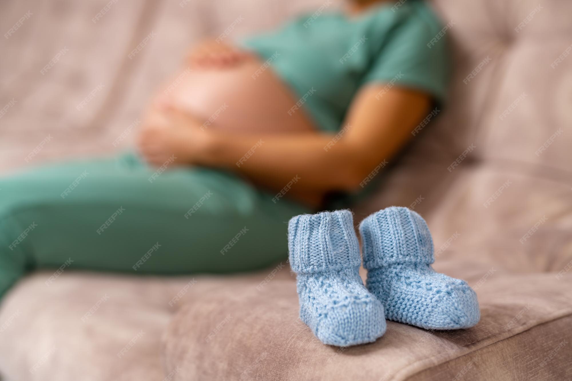 Petits Chaussons De Bebe En Tricot Bleu Pour Futur Garcon Nouveau Ne Petites Chaussettes De Bebe Sur Le Canape Image Floue D Une Femme Enceinte Assise Sur Un Canape En Toile De Fond Photo Premium