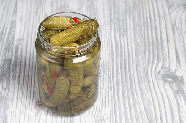 Petits concombres marinés dans un bocal en verre sur une table en bois