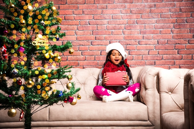 Petits enfants asiatiques indiens mignons célébrant Noël à la maison avec le chapeau de père Noël, les cadeaux et l'arbre de Noël