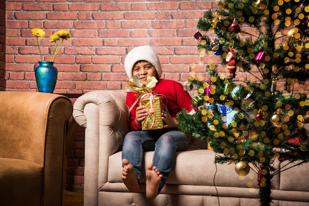 Petits enfants asiatiques indiens mignons célébrant Noël à la maison avec le chapeau de père Noël, les cadeaux et l'arbre de Noël