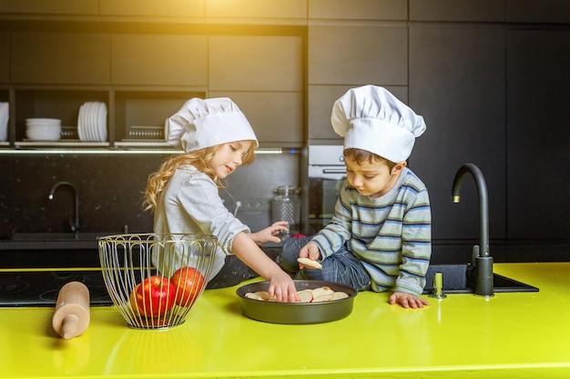 Petits enfants fille et garçon avec chapeau de chef préparant cuire une tarte aux pommes maison dans la cuisine frère et sœur