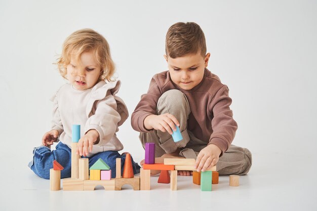 Petits enfants frère et soeur souriant s'amusant et jouant des jouets de briques colorées sur fond blanc Les enfants ont le sourire et s'amusent ensemble