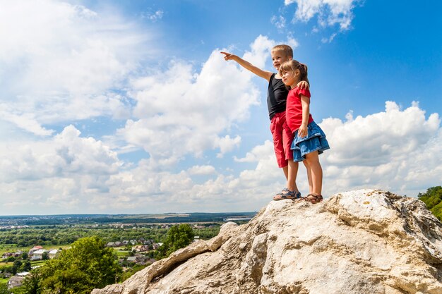 Petits enfants garçon et fille debout sur un rocher de montagne et regardant vers l'avenir. Garçon, projection, sien, main