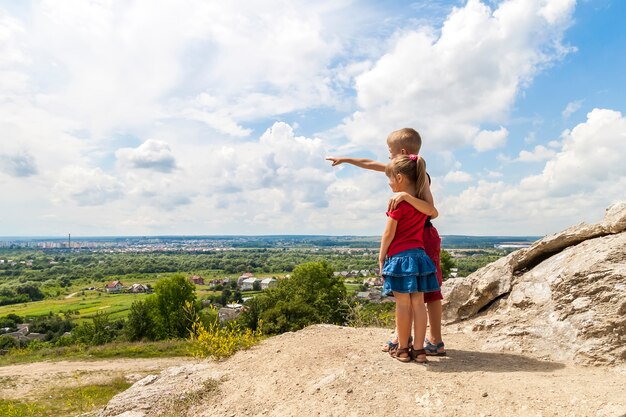 Petits enfants garçon et fille debout sur le rocher de la montagne et regardant vers l'avenir. Garçon, projection, sien, main