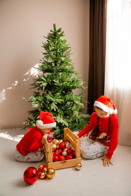 de petits enfants heureux en pyjama rouge décorent un arbre de Noël dans le concept d'hiver du salon