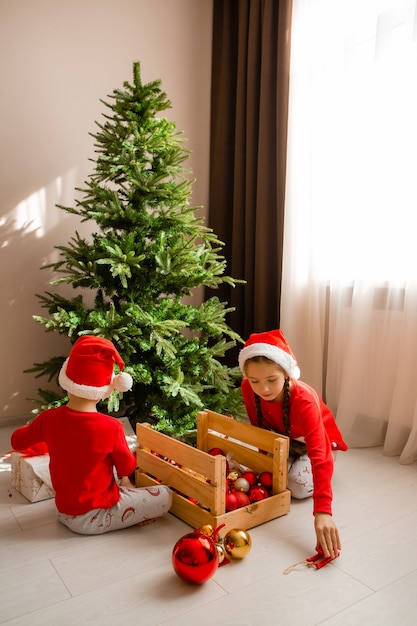 de petits enfants heureux en pyjama rouge décorent un arbre de Noël dans le concept d'hiver du salon