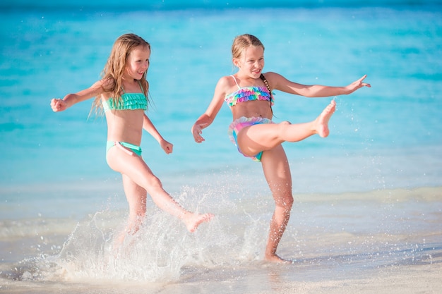 Les petits enfants heureux s'amusent beaucoup sur la plage tropicale en jouant ensemble en eau peu profonde.