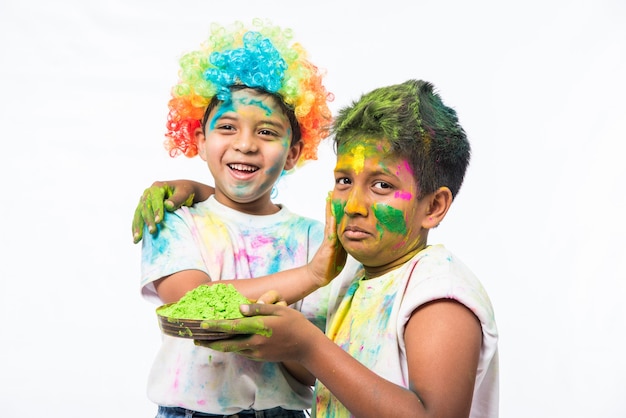 Petits enfants indiens ou amis ou frères et sœurs célébrant le festival Holi avec de la couleur gulal ou en poudre, des bonbons, du pichkari ou du spray, isolés sur fond blanc