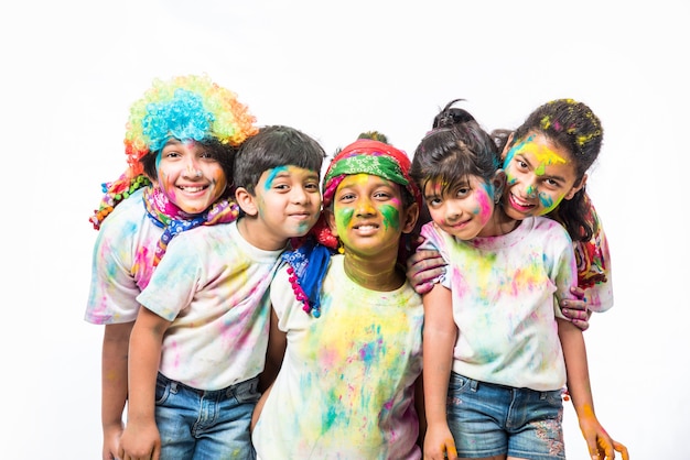 Petits enfants indiens ou amis ou frères et sœurs célébrant le festival Holi avec de la couleur gulal ou en poudre, des bonbons, du pichkari ou du spray, isolés sur fond blanc