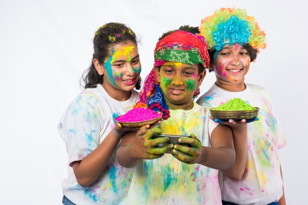 Petits enfants indiens ou amis ou frères et sœurs célébrant le festival Holi avec de la couleur gulal ou en poudre, des bonbons, du pichkari ou du spray, isolés sur fond blanc