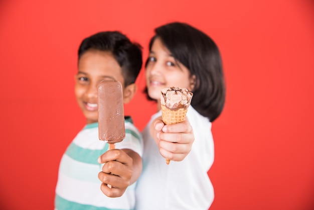 Petits enfants indiens ou asiatiques mignons mangeant de la crème glacée ou de la barre de mangue ou des bonbons. Isolé sur fond coloré