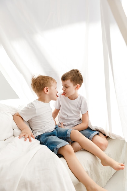 Petits enfants jouant sur un lit et s'amusant dans une hutte en draps.