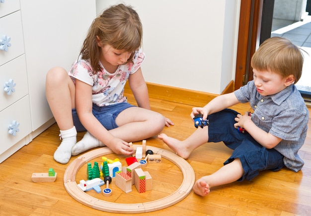 Petits enfants jouant avec un train en bois dans la chambre