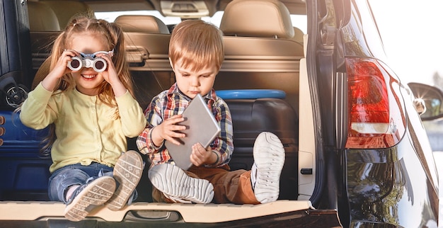 Petits enfants mignons s'amusant dans le coffre d'une voiture noire avec une famille de valises