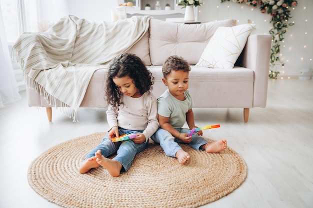 Petits enfants noirs afro-américains jouant avec des jouets pop sur le sol à la maison