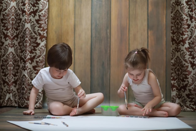 Les petits enfants peignent sur une grande feuille de papier au sol