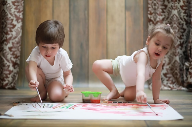 Les petits enfants peignent sur une grande feuille de papier au sol