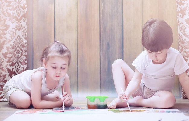 Les petits enfants peignent sur une grande feuille de papier sur le sol