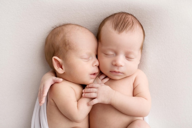 Petits garçons jumeaux nouveau-nés dans des cocons blancs sur fond blanc Un jumeau nouveau-né dort à côté de son frère Nouveau-né deux garçons jumeaux s'étreignant Photographie de studio professionnel