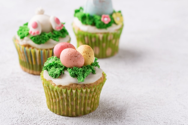 Petits gâteaux de fête avec des œufs de mastic et de l'herbe sur fond clair. Concept de vacances de Pâques. Espace de copie