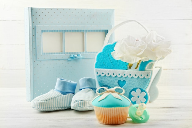 Petits gâteaux savoureux avec arc et chaussures de bébé, landau décoratif et album photo sur fond de couleur