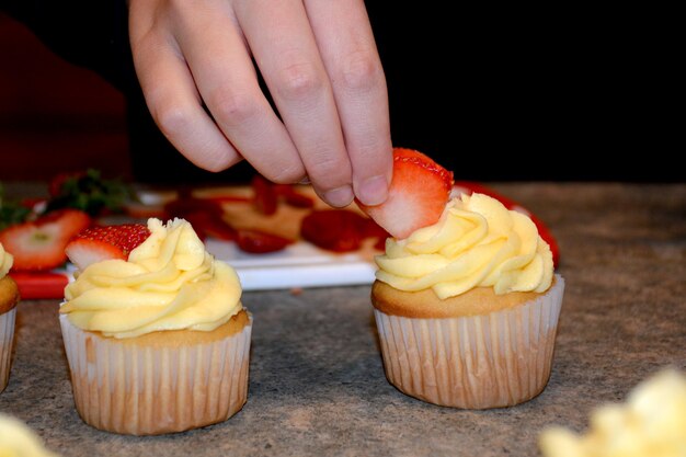Petits gâteaux savoureux avec la crème au beurre Personne décorant le petit gâteau avec la fraise