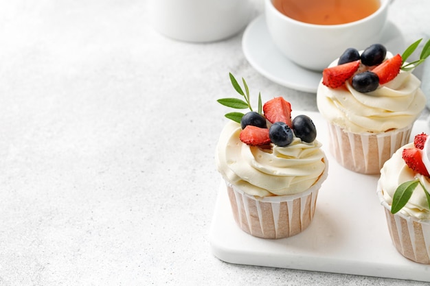 Petits gâteaux à la vanille avec crème au beurre et baies fraîches sur fond gris avec thé Dessert maison