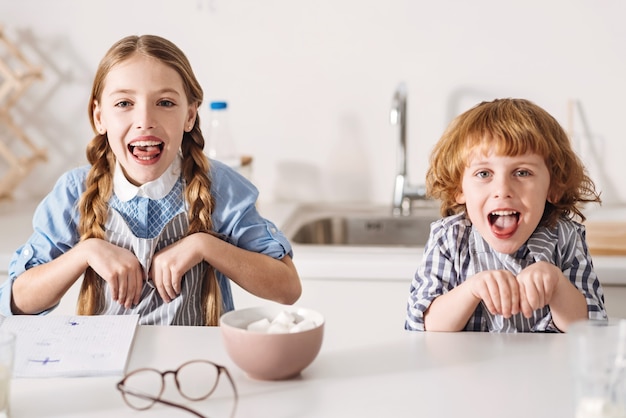 Petits lapins. Frères et sœurs artistiques positifs amusants faisant des grimaces imitant des lapins alors qu'il était assis à la table dans une cuisine spacieuse et ensoleillée