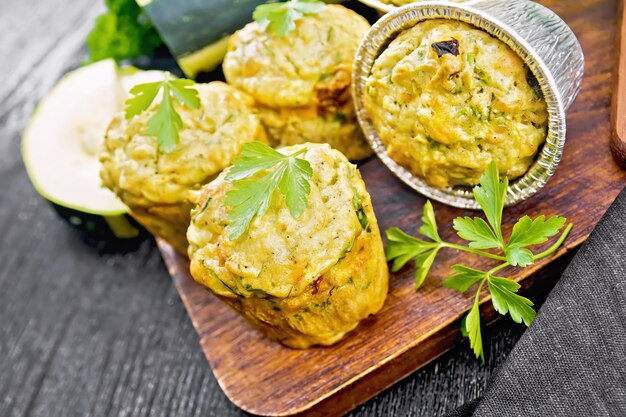 Petits muffins au fromage et aux courgettes avec des herbes, du persil, du thym, un couteau et une serviette sur fond de planche de bois foncé