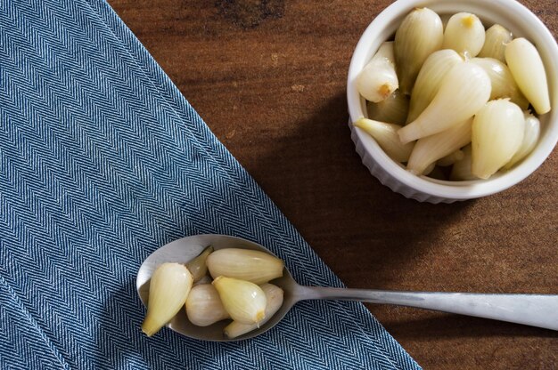 Petits oignons marinés dans une cuillère sur un chiffon bleu et un bol blanc avec plus d'oignons