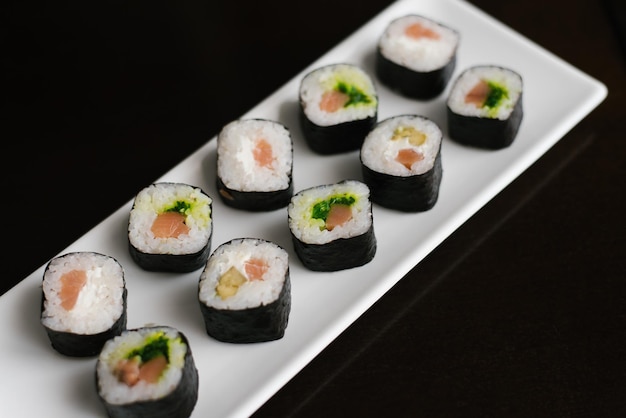 Des petits pains au saumon et à la salade de chuka se trouvent sur une assiette rectangulaire blanche