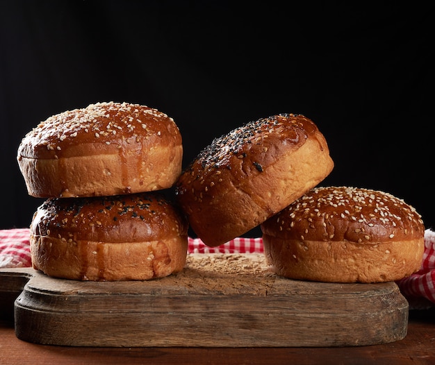 Petits pains au sésame croustillants cuits au four pour hamburgers sur planche de bois brun