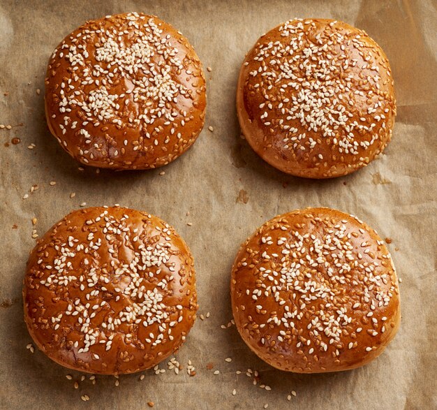 Petits pains au sésame cuits au four sur papier parchemin brun, ingrédient pour un hamburger, vue du dessus