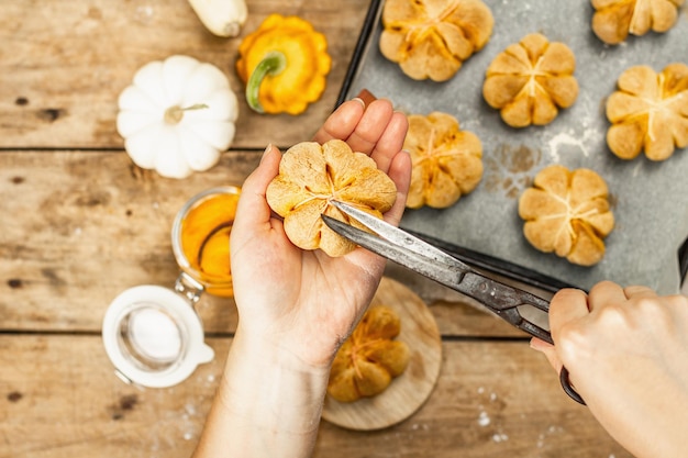 Petits pains ou biscuits à la citrouille, produits de boulangerie traditionnels d'automne. Les mains des femmes tiennent des cookies. Cuisine maison de saison et déco automnale. Vieux fond de planches de bois, vue de dessus