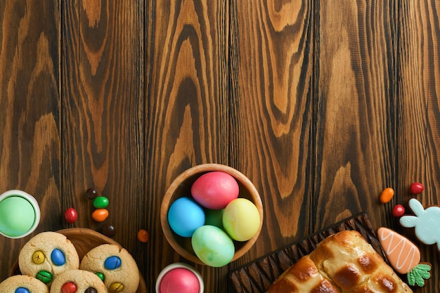 Petits pains chauds de Pâques avec des oeufs colorés Lapins de pain d'épice de Pâques et biscuits sur une planche en bois brun foncé vieux fond de table Concept de cuisson de vacances de printemps Réglage de la table de Pâques Vue de dessus Maquette