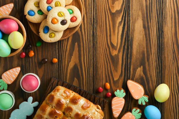 Petits pains chauds de Pâques avec des oeufs colorés Lapins de pain d'épice de Pâques et biscuits sur une planche en bois brun foncé vieux fond de table Concept de cuisson de vacances de printemps Réglage de la table de Pâques Vue de dessus Maquette