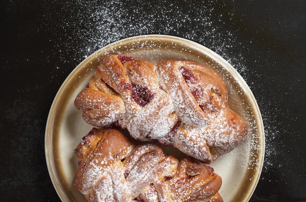 Petits pains avec confiture et sucre en poudre dans une assiette sur fond noir, vue de dessus