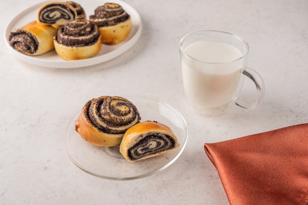 Petits pains faits maison aux graines de pavot sur une assiette blanche, tasse avec du lait sur un fond clair close-up.