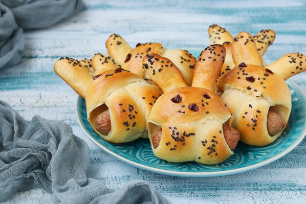 Petits pains en forme de lièvres avec des saucisses sont situés sur une assiette sur une surface bleue, idée culinaire pour les enfants, gros plan