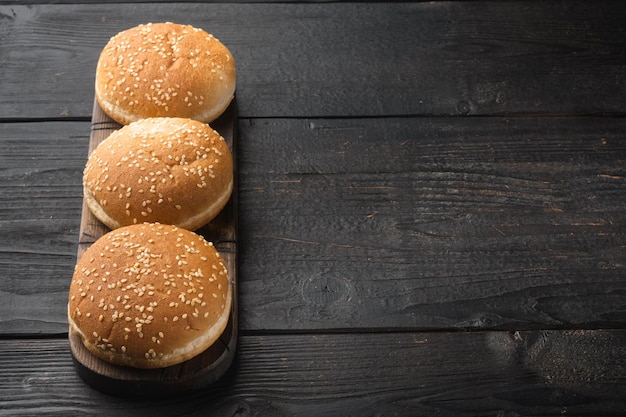 Petits pains à hamburger frais faits maison au sésame sur une planche de service en bois sur fond de table en bois noir avec espace de copie pour le texte