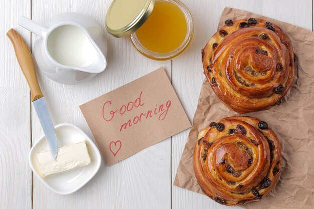 Petits pains savoureux aux raisins secs avec du lait de beurre et du miel sur un fond en bois blanc petit-déjeuner de boulangerie frais vue d'en haut