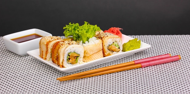 Petits pains savoureux servis sur une assiette blanche avec des baguettes sur un tapis gris sur fond gris