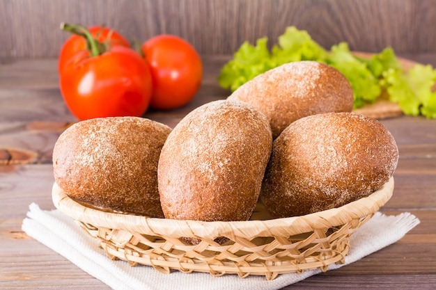 Petits pains de seigle frais dans un panier, salade et tomates sur une table en bois