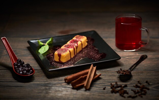 Petits pains sucrés dans une assiette noire servant avec un brin de menthe sauce Verre de cuillère à thé avec des bleuets épices Fond sombre