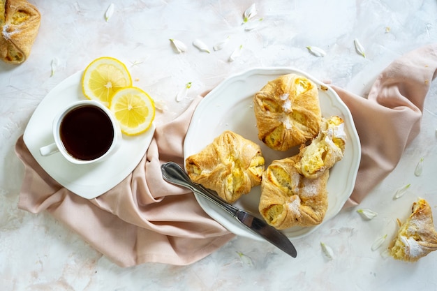 Petits pains sucrés de pâte feuilletée de gâteaux faits maison avec la tasse de thé de fromage cottage